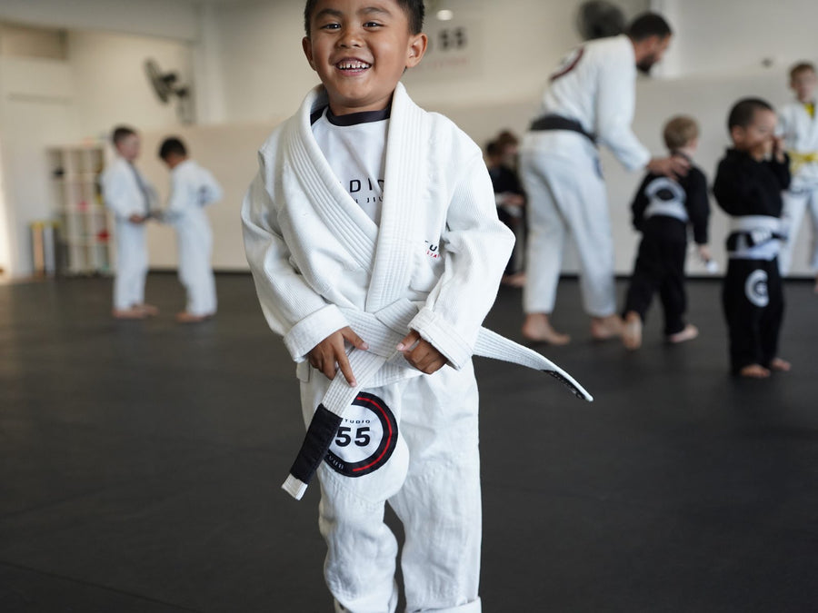 Smiling young student in a white gi at Studio 55 Kids BJJ class for ages 4 to 5 in Loganholme